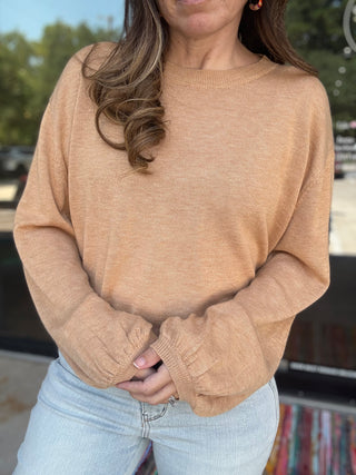 Person wearing a beige sweater and light blue jeans outdoors- ava wray boutique