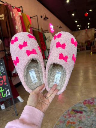 Pink slippers with pink bows held by a hand in a blurred indoor setting