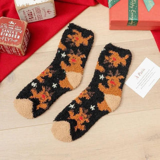 Pair of festive socks with reindeer pattern on a wooden surface with Christmas-themed items.