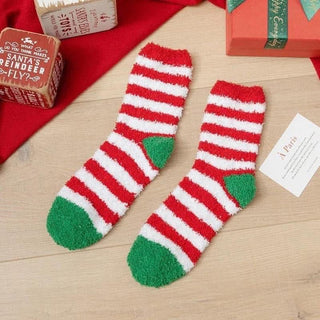 Red and green striped socks on a wooden surface with Christmas-themed boxes in the background.