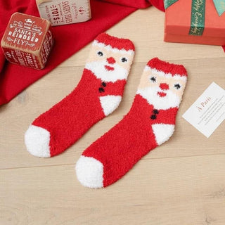 Red Santa Claus socks on a wooden surface with Christmas-themed boxes and cards.