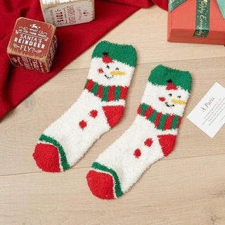 Pair of snowman-themed socks on a wooden surface with Christmas decorations.