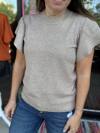 Person wearing a beige sweater and blue jeans in an outdoor setting-ava wray boutique