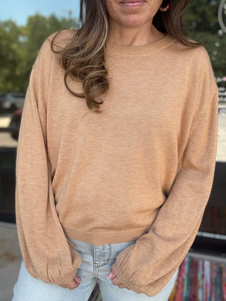 Woman wearing a beige sweater with a blurred outdoor background- ava wray boutique