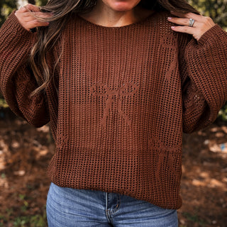 Person wearing a brown knitted sweater with a logo, standing outdoors.-ava wray boutique