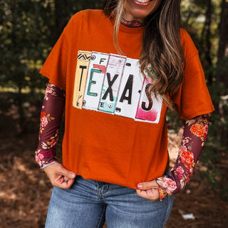 Person wearing an orange t-shirt with a Texas license plate design, floral sleeves, and blue jeans-ava wray boutique