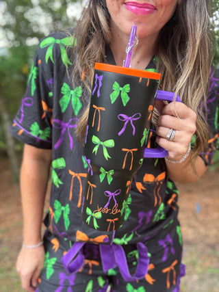 Person wearing a black outfit with colorful bows and holding a matching cup-ava wray boutique