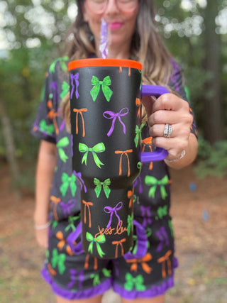 Person holding a black mug with colorful bows and the text 'Jess Lee' outdoors-ava wray boutique