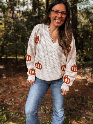 Woman wearing a white sweater with orange pumpkin patterns outdoors-ava wray boutique
