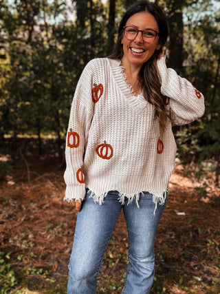 Woman wearing a cream sweater with pumpkin patterns in an outdoor setting-ava wray boutique