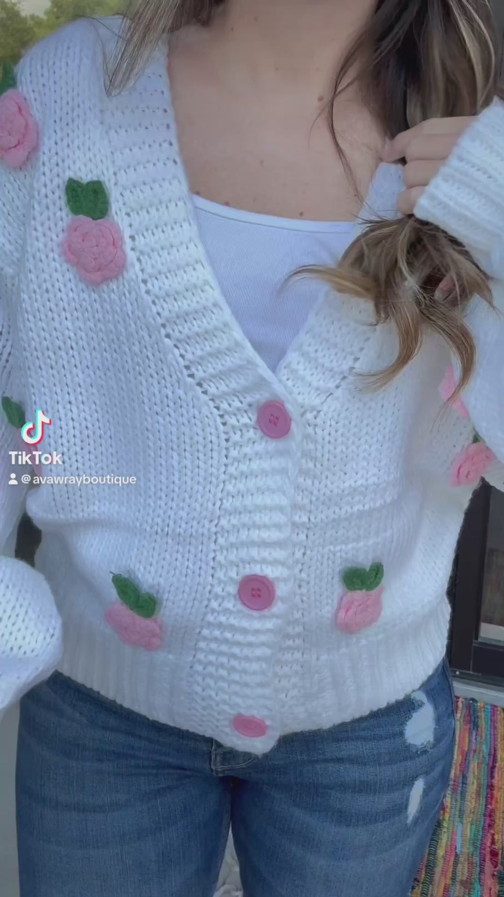 Person wearing a white knitted cardigan with pink floral patterns outdoors-ava wray boutique