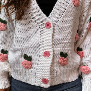Knitted cardigan with pink buttons and embroidered pink flowers on a person wearing it-ava wray boutique