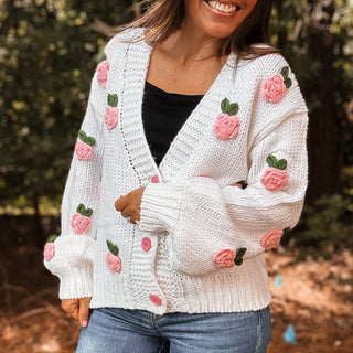 Person wearing a white knitted cardigan with pink floral patterns outdoors-ava wray boutique