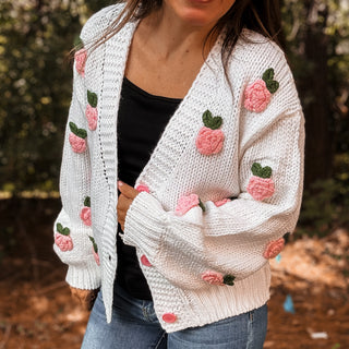Person wearing a white knitted cardigan with pink floral patterns outdoors-ava wray boutique